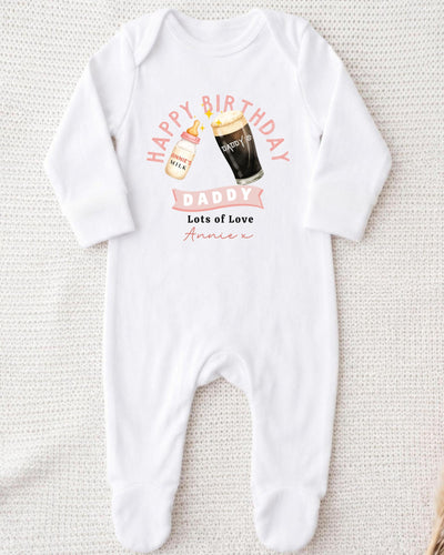 A white onesie with a graphic design on it, featuring a bottle of milk and a glass of beer, along with the text "Happy Birthday Daddy Lots of Love Annie" printed on it.
