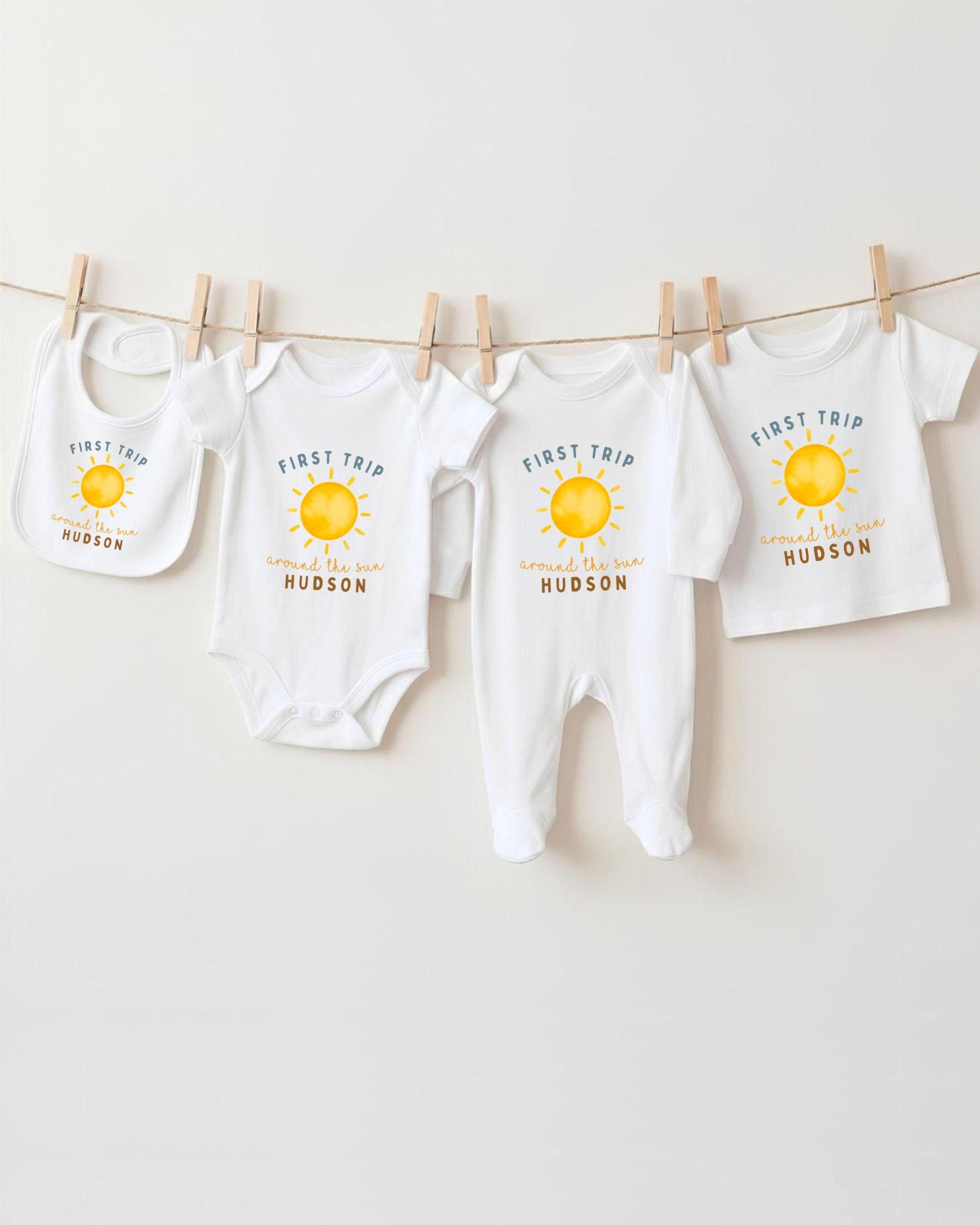 A collection of baby clothes, including onesies and bibs, hanging on a clothesline.