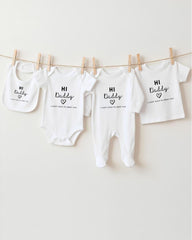 a collection of four white baby clothes hanging on a clothesline, each with a unique message printed on it.
