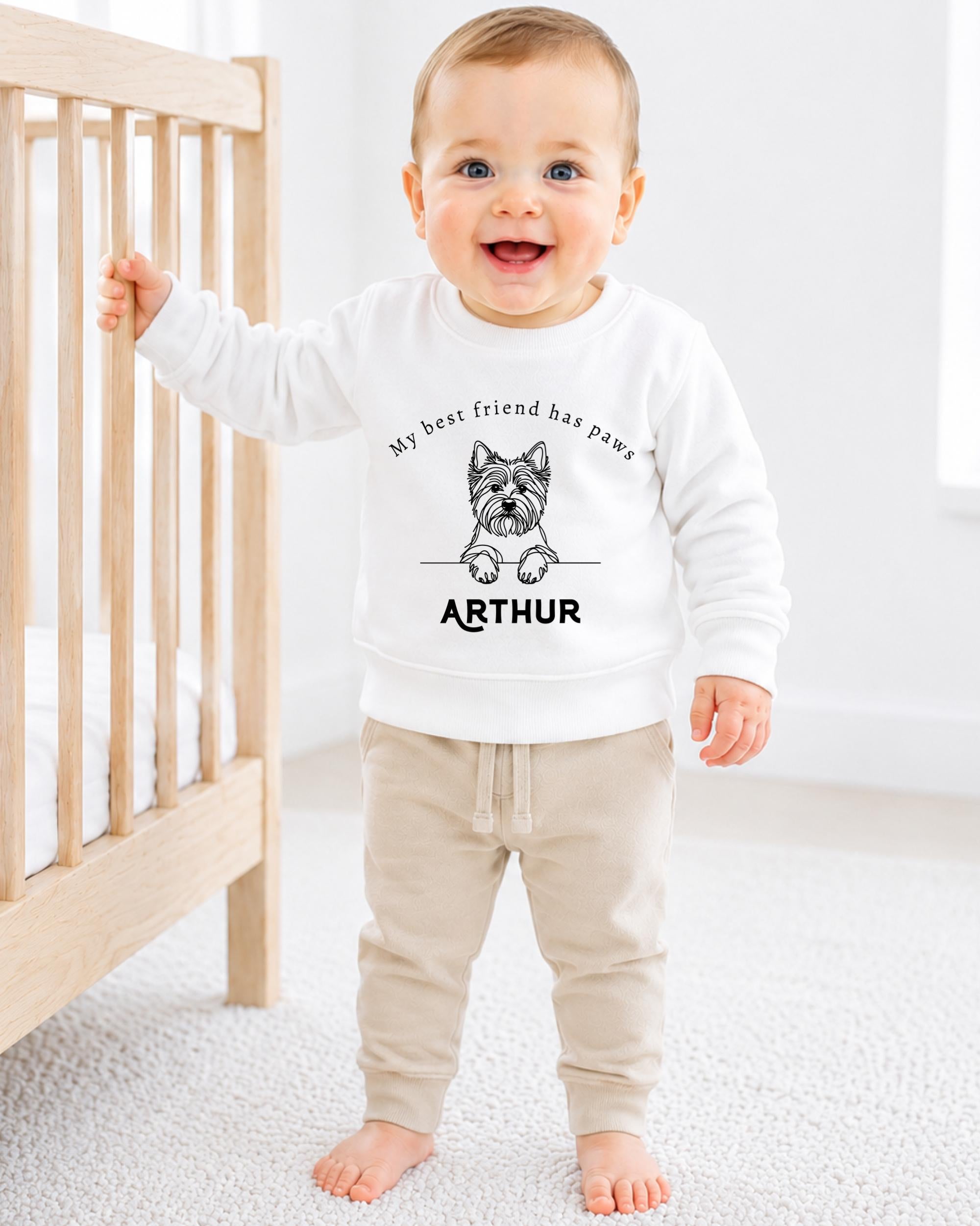 A smiling baby boy wearing a white sweatshirt with a dog graphic and the name "Arthur" printed on it.