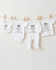 A row of four white baby clothes with black text and illustrations, hanging on a clothesline.