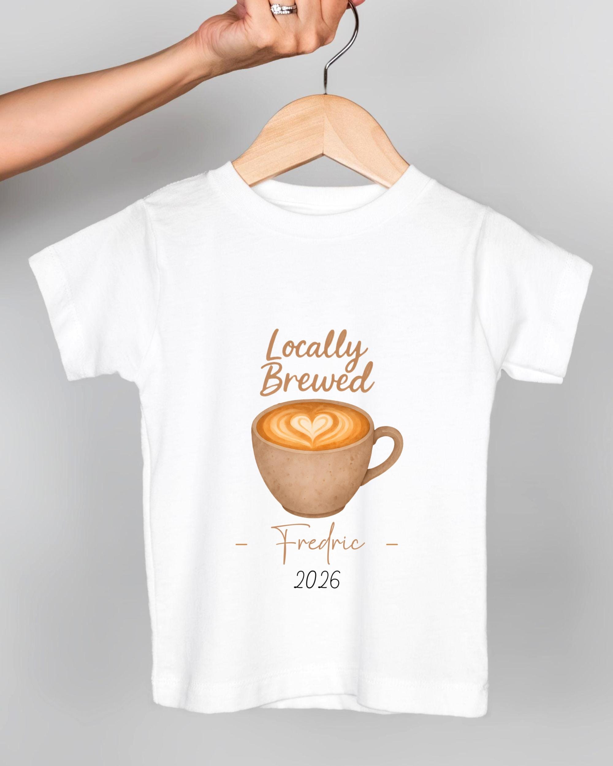 A white t-shirt with a graphic design of a cup of coffee and the text "Locally Brewed Fredric 2026" printed on it.