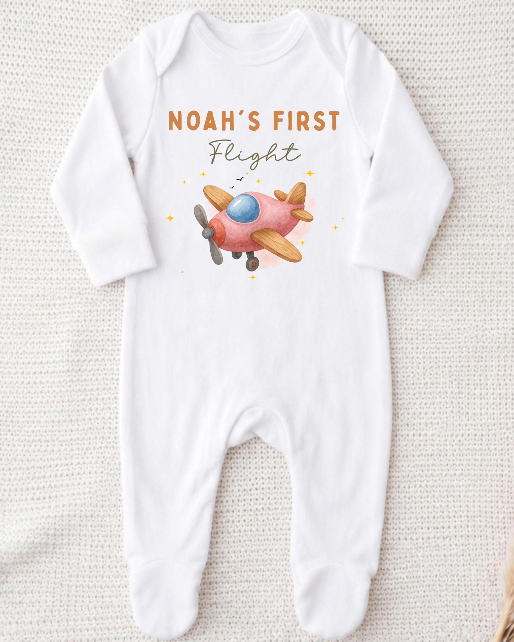 A white onesie with a pink airplane printed on it, along with the text "Noah's first flight" printed above the airplane.