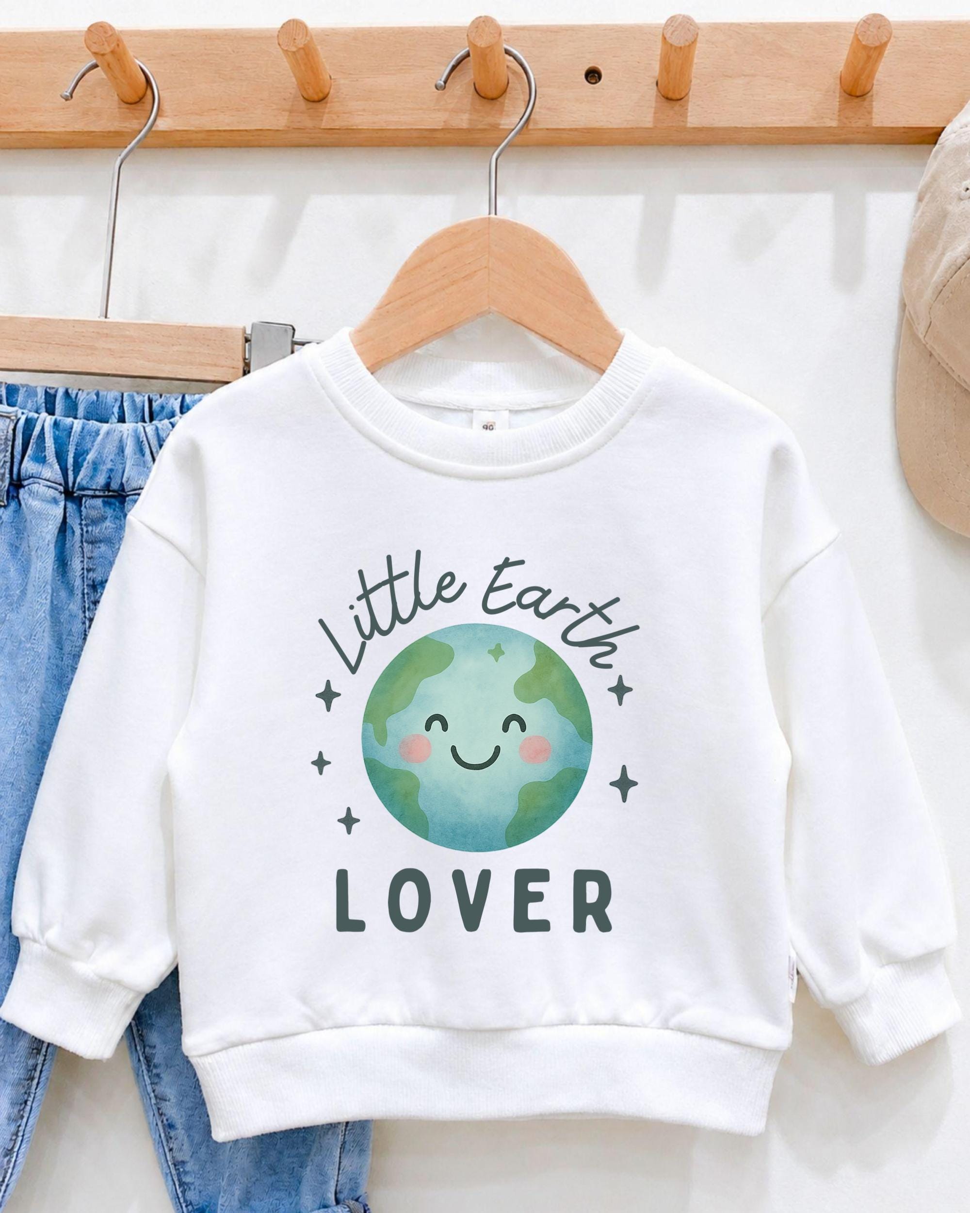A white sweatshirt with a cartoon image of a smiling Earth and the text "Little Earth Lover" printed on it, hanging on a wooden hanger.