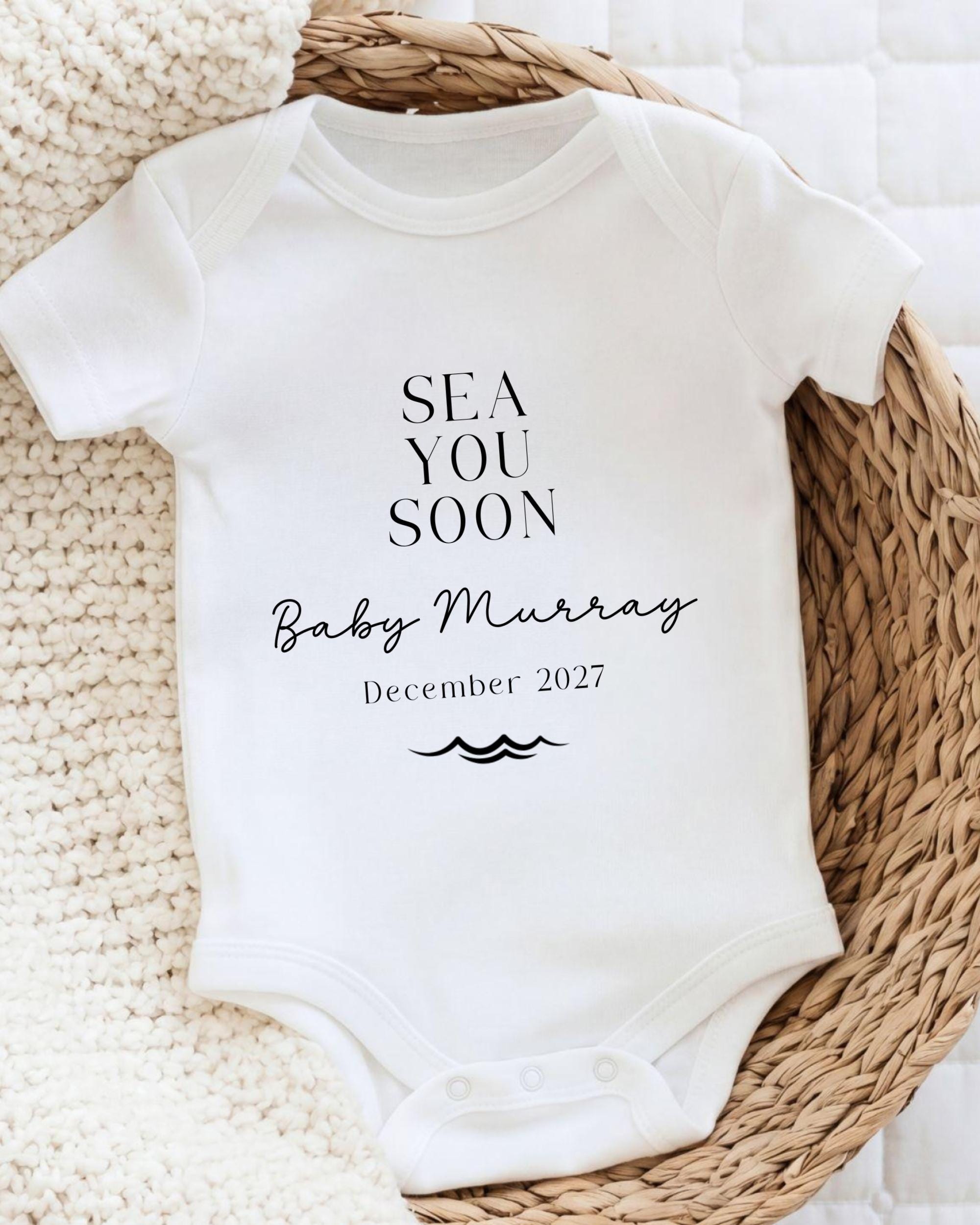 A white baby onesie with text printed on it, placed on a woven basket.
