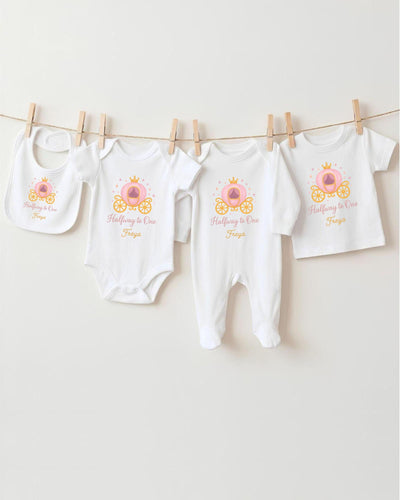 A row of four white baby clothes with a princess-themed design, including a princess carriage, is hanging on a clothesline.