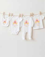 A row of four white baby clothes with a princess-themed design, including a princess carriage, is hanging on a clothesline.