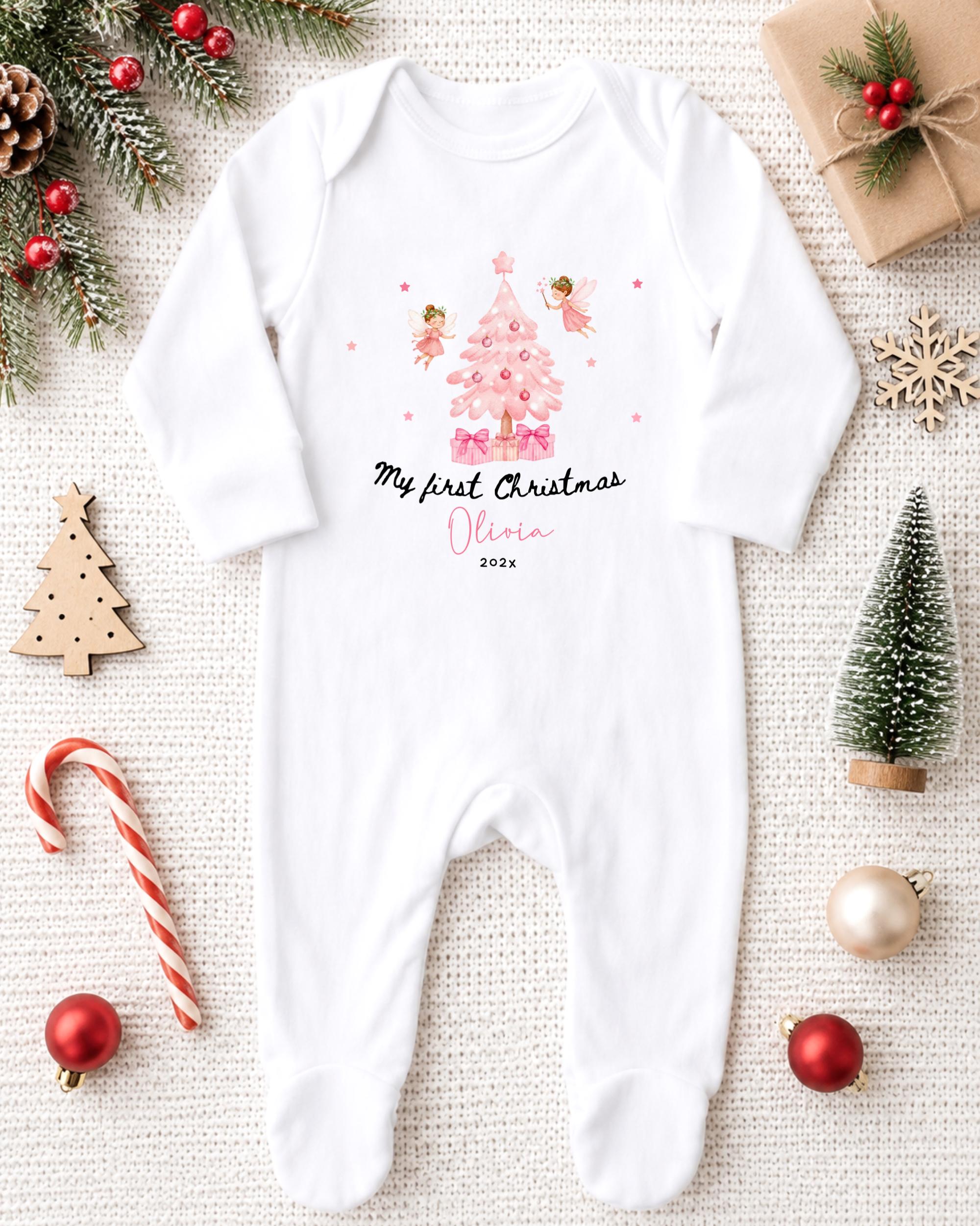 A white onesie with a Christmas tree design and two small angels, along with other Christmas decorations, is displayed on a white background.
