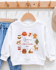 A white sweatshirt with a Christmas-themed design hanging on a wooden hanger.