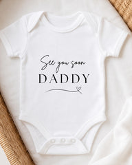 A white baby onesie with the text "See you soon Daddy" printed on it.