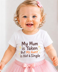A smiling baby girl wearing a white t-shirt with text and a pink bow in her hair.