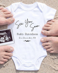 a white onesie with the text "Sea You Soon Baby Davidson Due December 2026" written on it, along with a black and white photograph of a baby's belly.