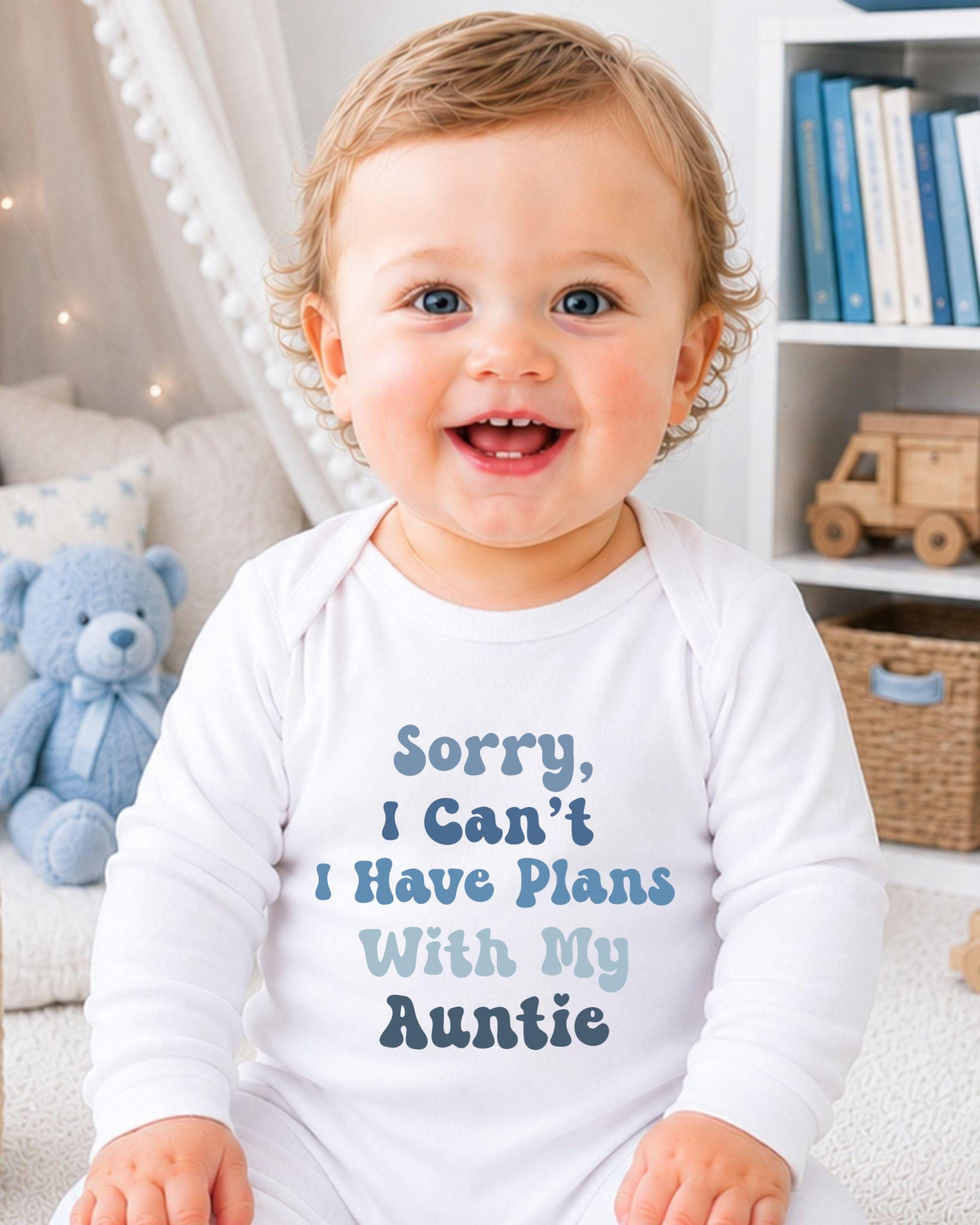 A smiling baby wearing a white onesie with text that says "Sorry, I Can't I Have Plans With My Auntie" is sitting in a room with a teddy bear and bookshelf in the background.