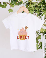 A white t-shirt with a cupcake design and the name "EMILY" printed on it, hanging on a wooden hanger.