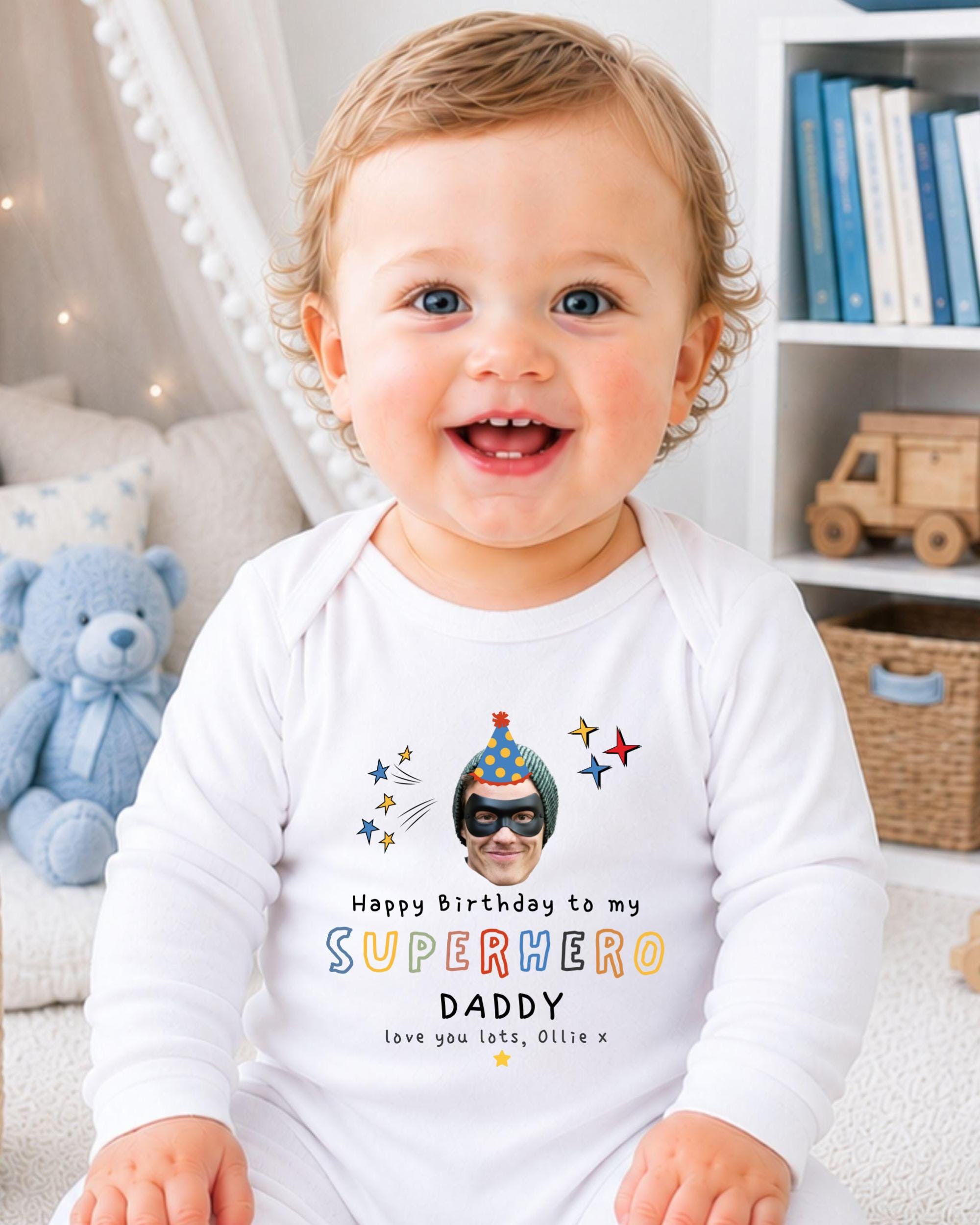 A smiling baby wearing a white onesie with a personalized birthday message and a superhero image.