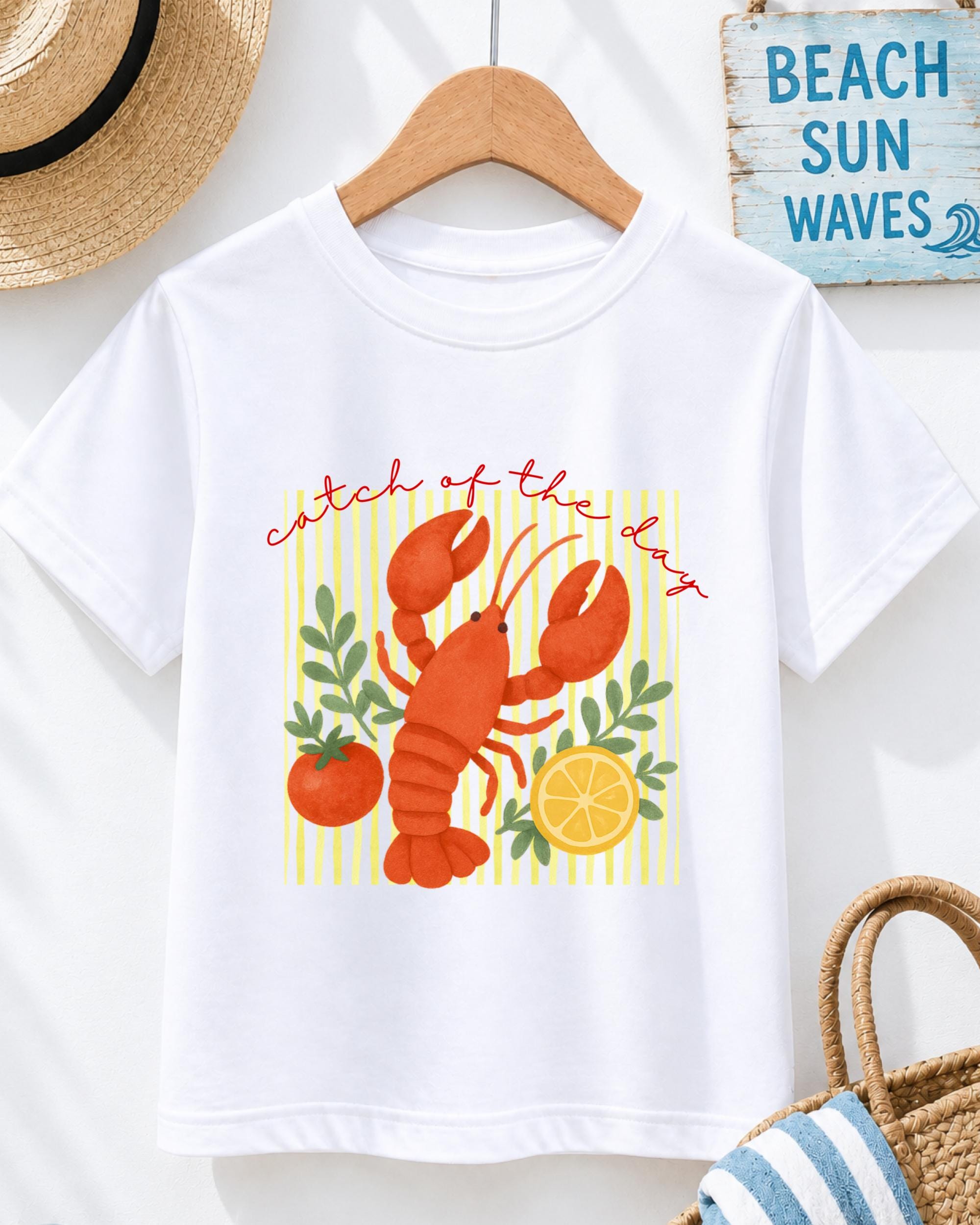A white t-shirt with a colorful illustration of a lobster and various fruits, including an orange and a lemon, along with the text "Catch of the day" printed on it.