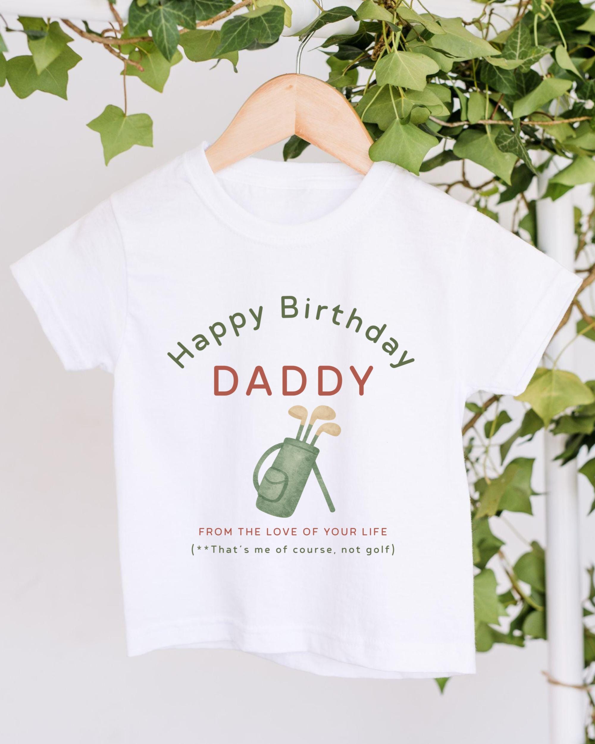 A white t-shirt with a graphic design and text printed on it, hanging on a wooden hanger.