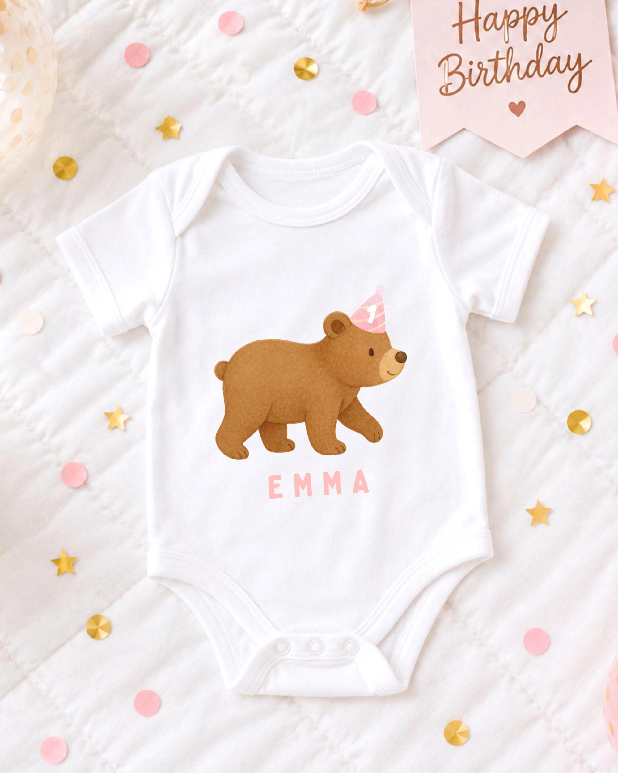 A white baby onesie with a bear design and the name "Emma" printed on it, along with a pink birthday banner and confetti.