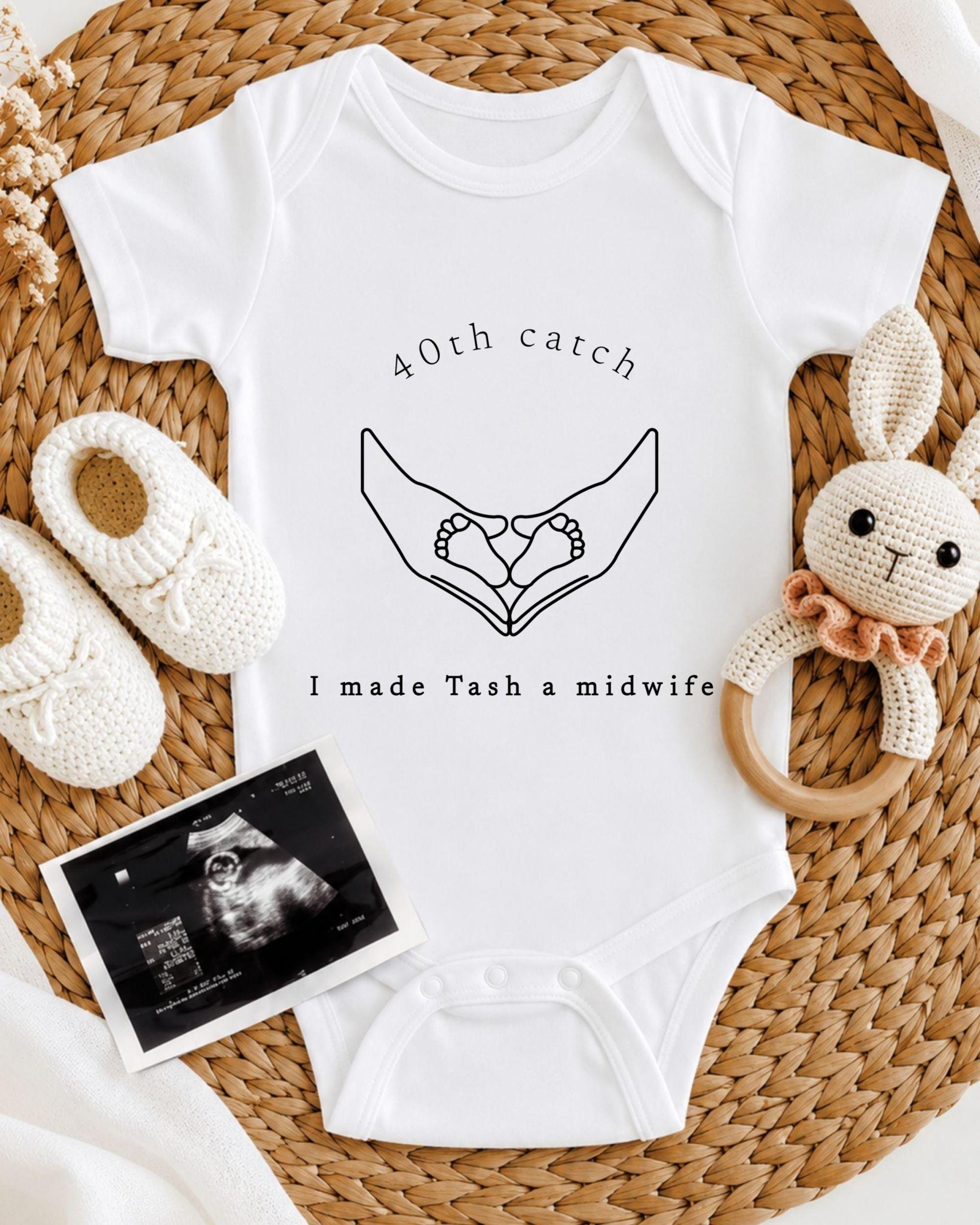 A white onesie with a graphic of hands holding baby feet, accompanied by a crocheted rabbit toy and a baby bootie. The image also includes an ultrasound image of a baby's feet.