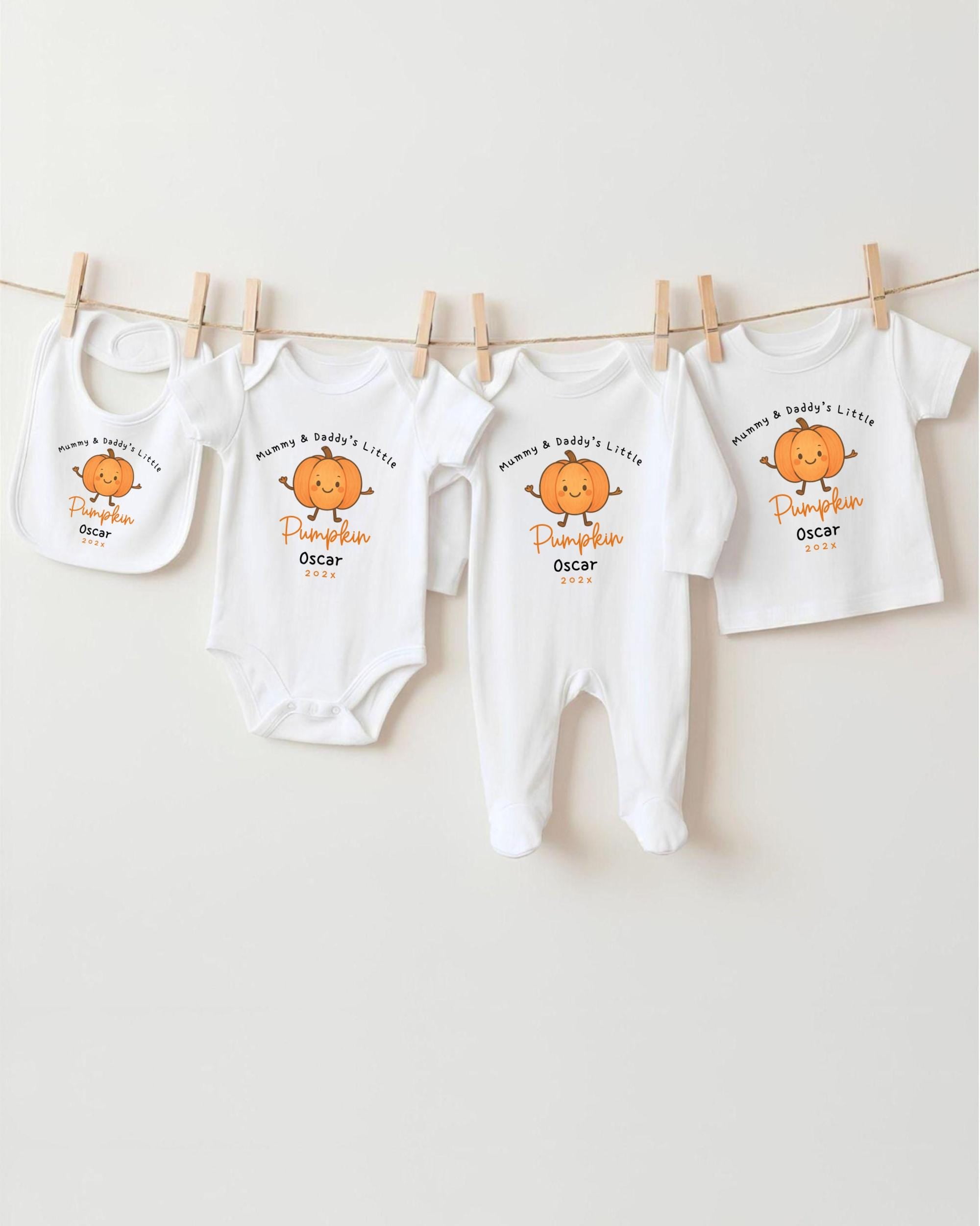 A row of four white baby clothes with orange pumpkin designs, each with a personalized name and age printed on them.