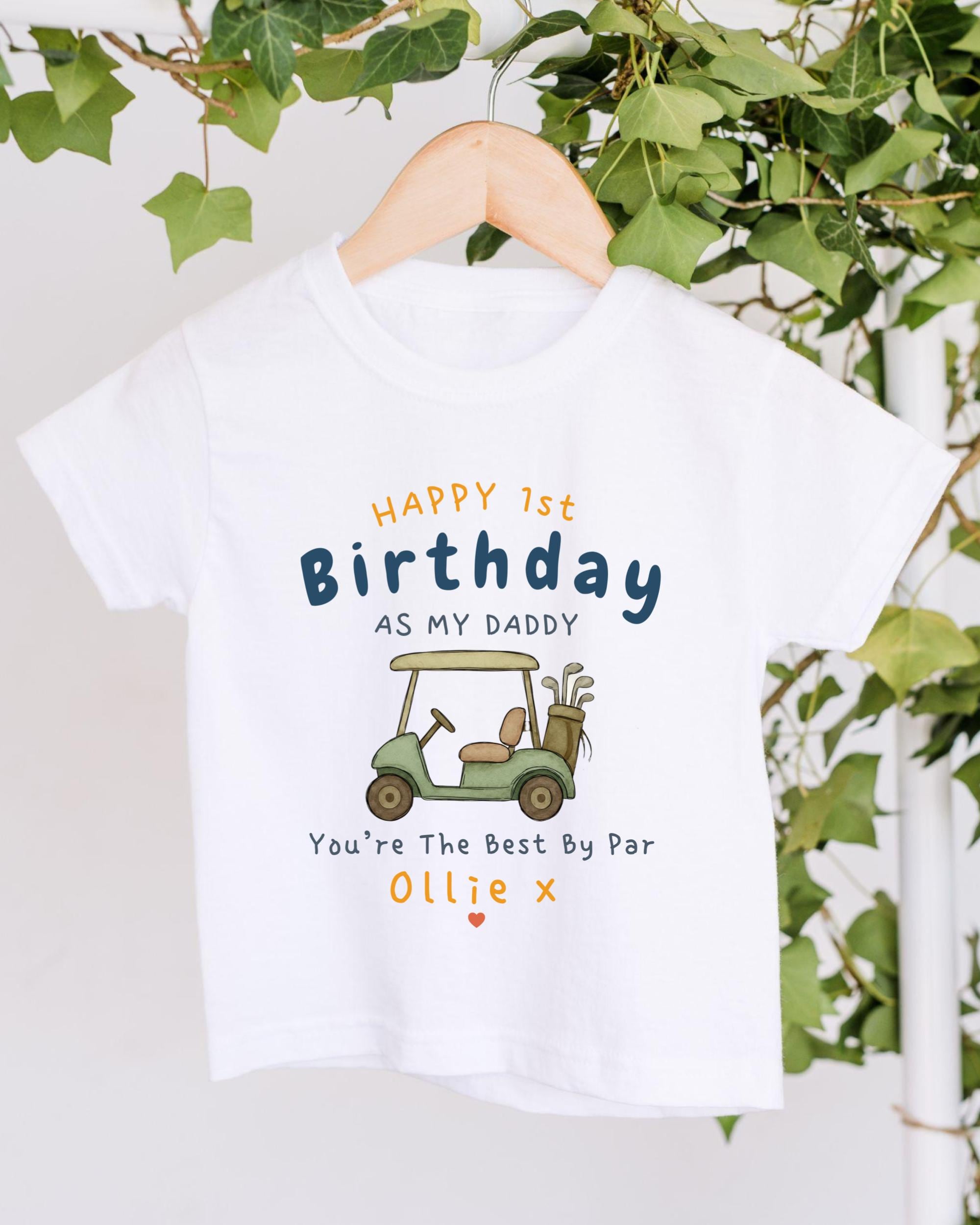A white t-shirt with a golf cart graphic and text printed on it, hanging on a wooden hanger.