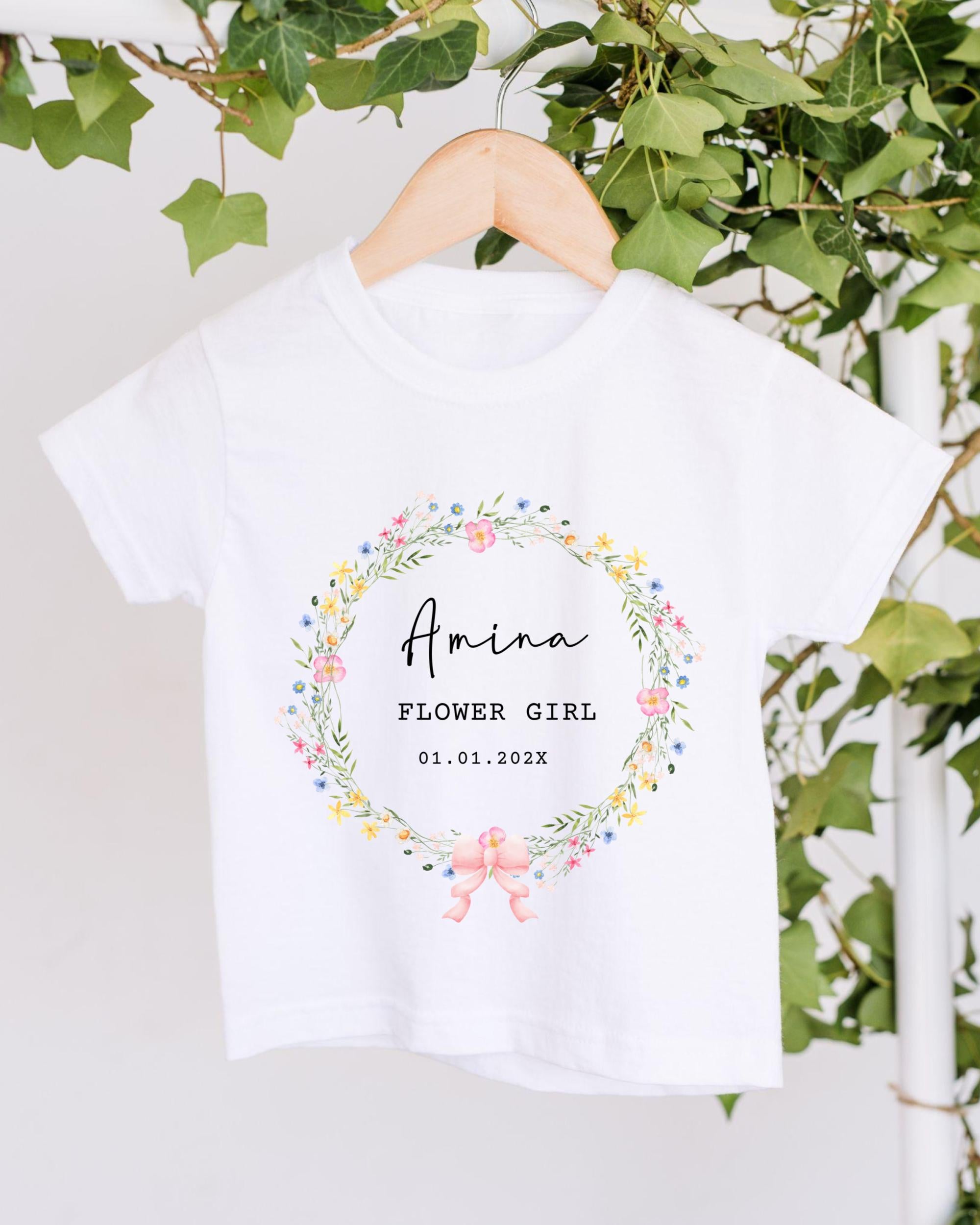 A white t-shirt with a floral wreath design and text printed on it, hanging on a wooden hanger.