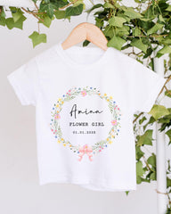 A white t-shirt with a floral wreath design and text printed on it, hanging on a wooden hanger.