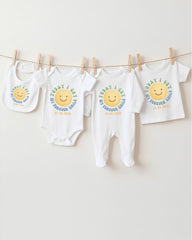 A row of four white baby clothes with a smiley face design, hanging on a clothesline.