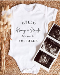 A white baby onesie with text that says "Hello Nanny & Grandpa See you in October" is displayed alongside a set of three black and white baby ultrasound images.