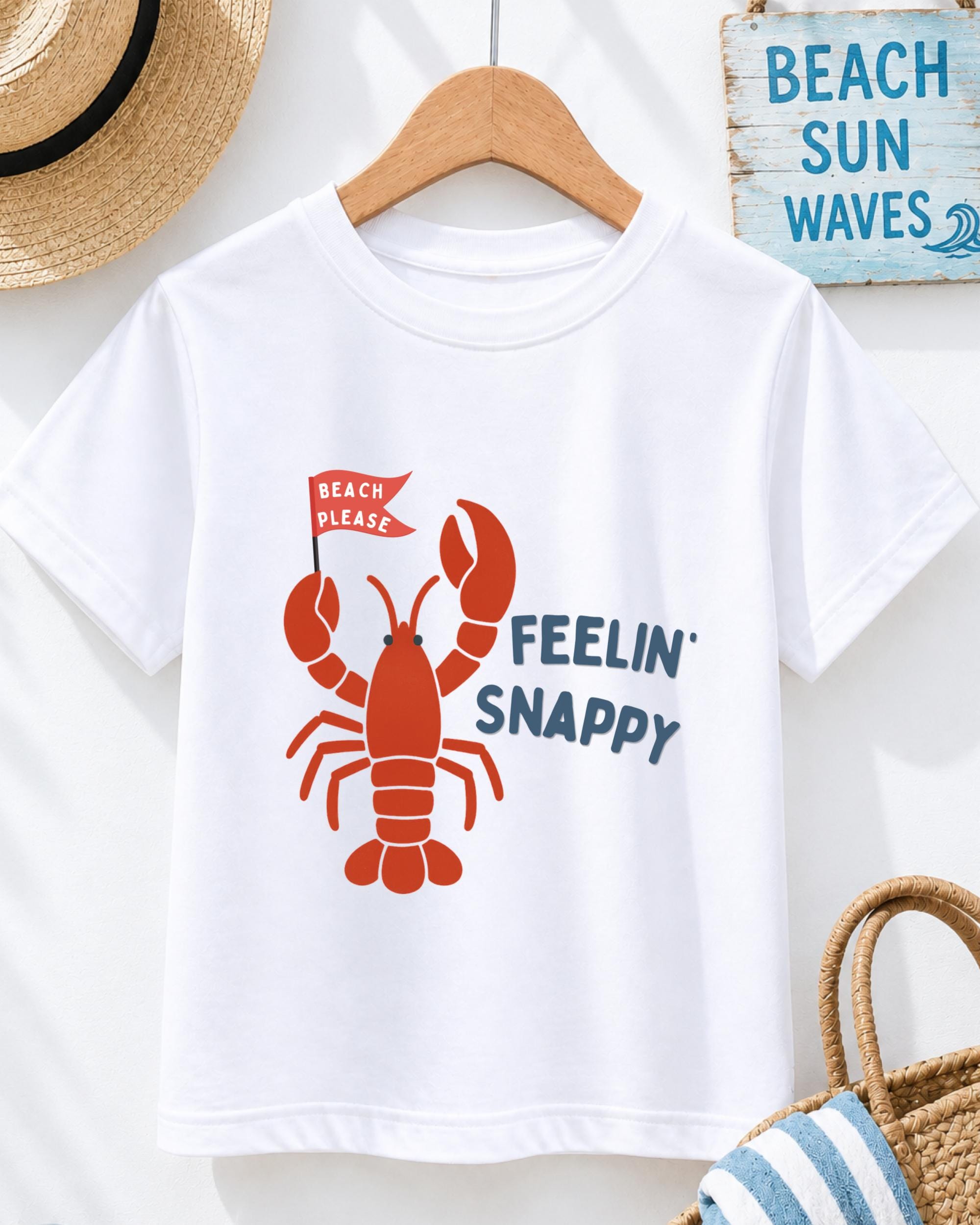 A white t-shirt with a red lobster graphic and the text "BEACH PLEASE FEELIN' SNAPPY" printed on it, along with a red flag. The t-shirt is hanging on a wooden hanger, and there is a straw hat and a blue sign with the text "BEACH SUN WAVE" on the wall behind it.