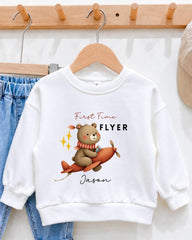 A white sweatshirt with a cartoon image of a bear on an airplane and the text "First Time Flyer Jason" printed on it.