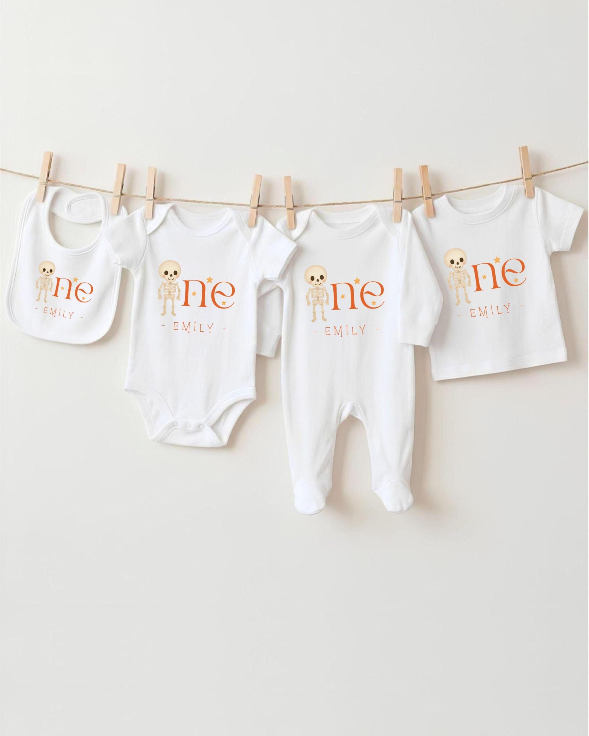 A row of four white baby clothes with the name "Emilly" printed on them, hanging on a clothesline.