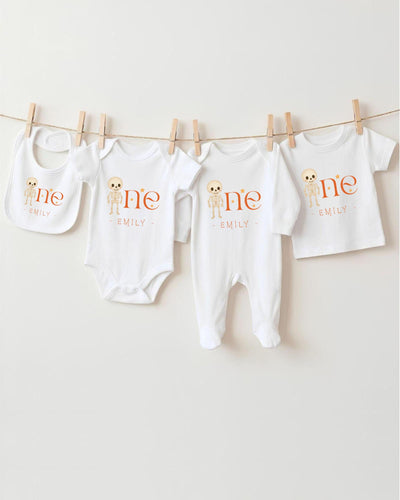 A row of four white baby clothes with the name "Emilly" printed on them, hanging on a clothesline.