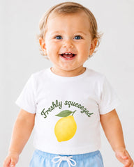 A smiling baby wearing a white t-shirt with a lemon graphic and the text "Freshly squeezed" printed on it.