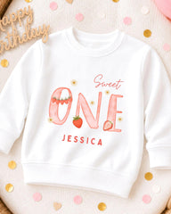 A white sweatshirt with a personalized design on it, featuring the text "Sweet One" and the name " Jessica".