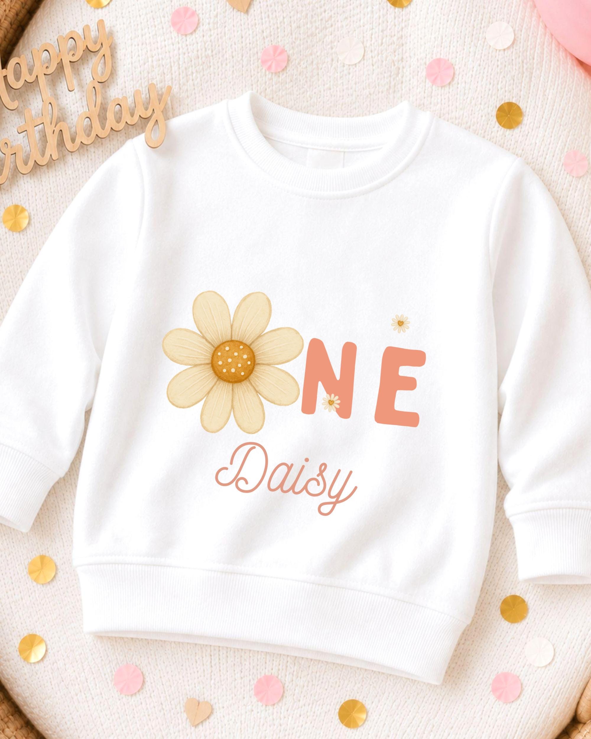 A white sweatshirt with a flower design and the text "ONE Daisy" printed on it, surrounded by confetti.