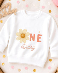 A white sweatshirt with a flower design and the text "ONE Daisy" printed on it, surrounded by confetti.