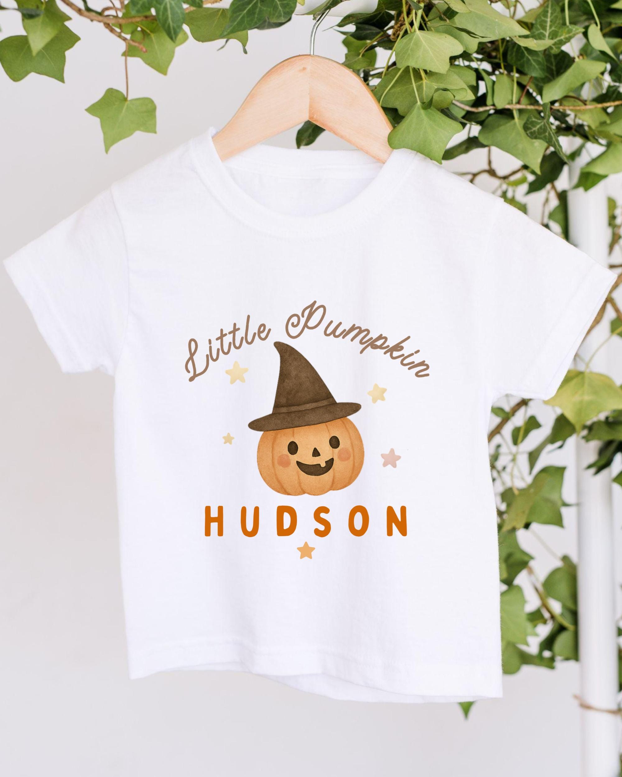 A white t-shirt with a pumpkin graphic and the text "Little Pumpkin" printed on it, along with the name "Hudson" below the pumpkin.