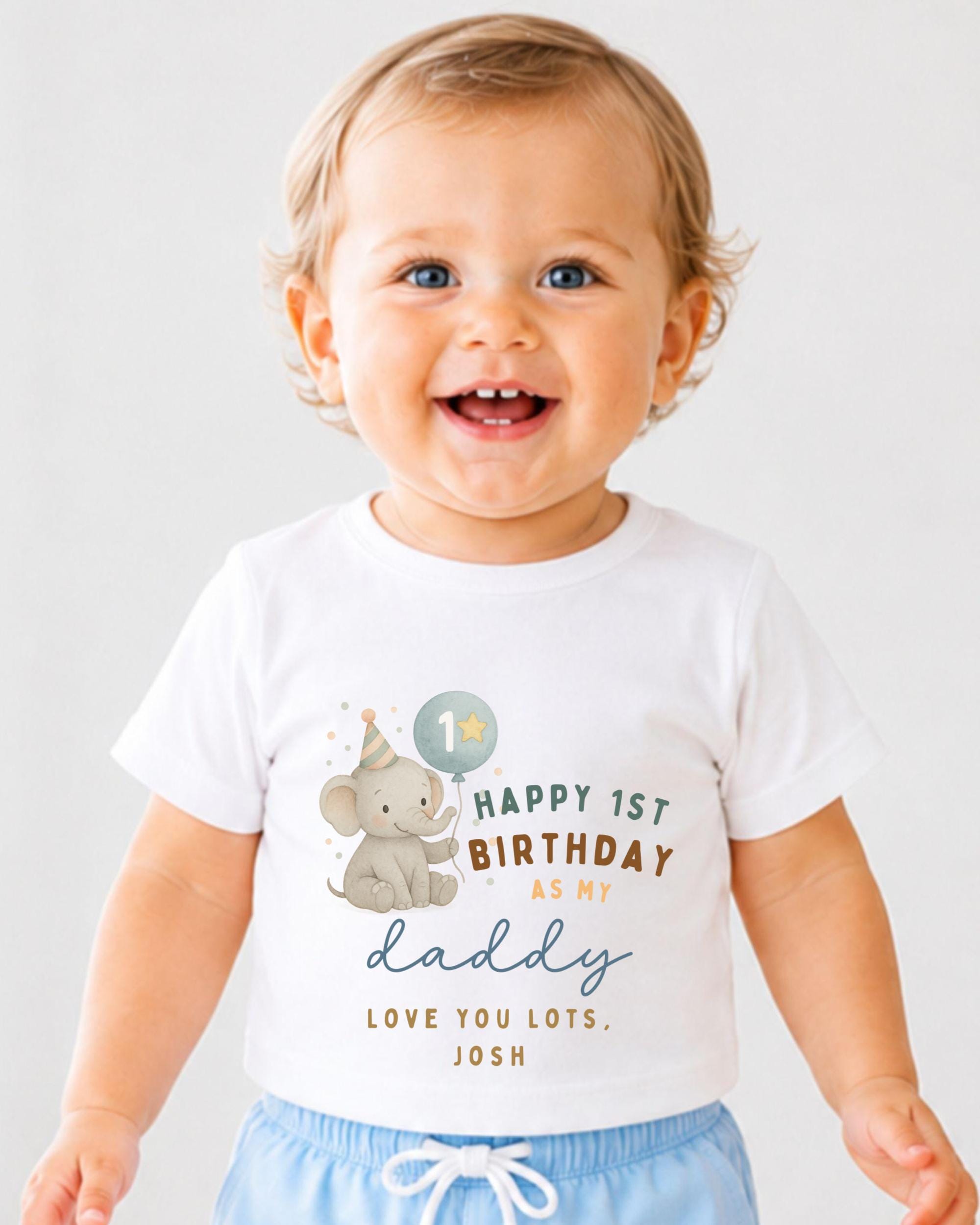 A smiling baby boy wearing a white t-shirt with a birthday message and an elephant graphic.