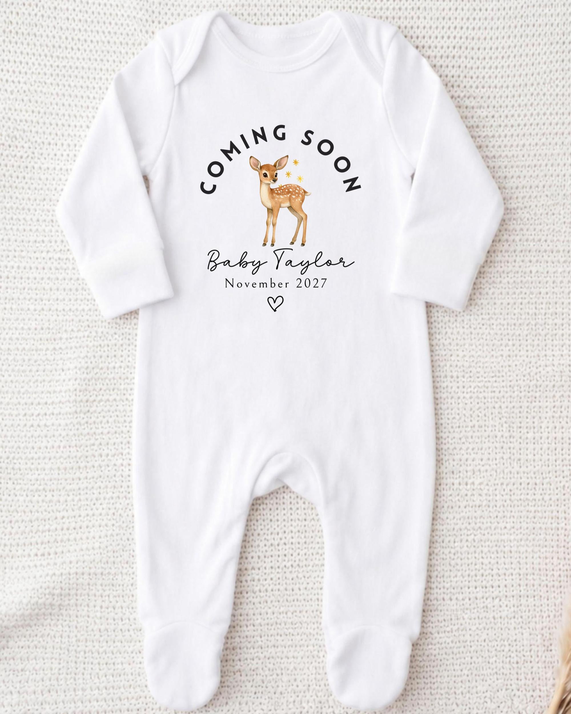 A white onesie with a graphic of a deer and text that announces the arrival of a baby named Baby Taylor.
