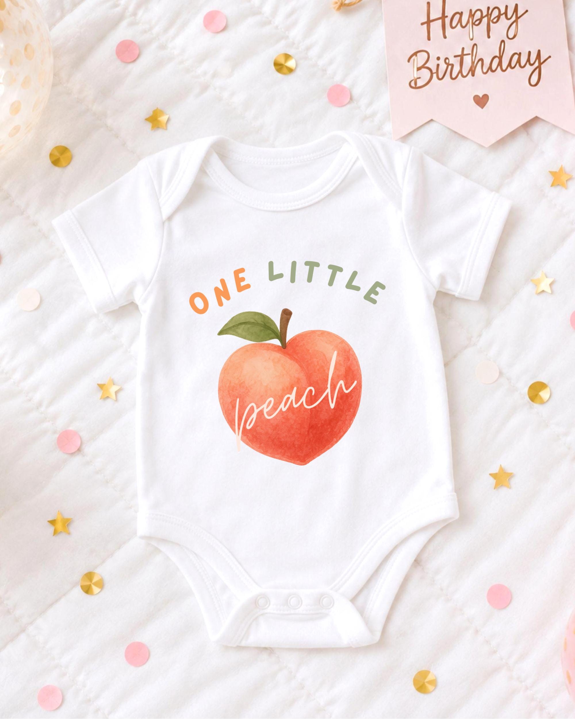 A white onesie with a peach design and the text "ONE LITTLE peach" printed on it, along with confetti and a "Happy Birthday" sign.