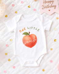 A white onesie with a peach design and the text "ONE LITTLE peach" printed on it, along with confetti and a "Happy Birthday" sign.
