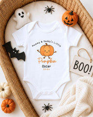 A white onesie with a pumpkin graphic and text, surrounded by Halloween decorations such as a ghost, a pumpkin, a bat, and a sign that says "BOO!".