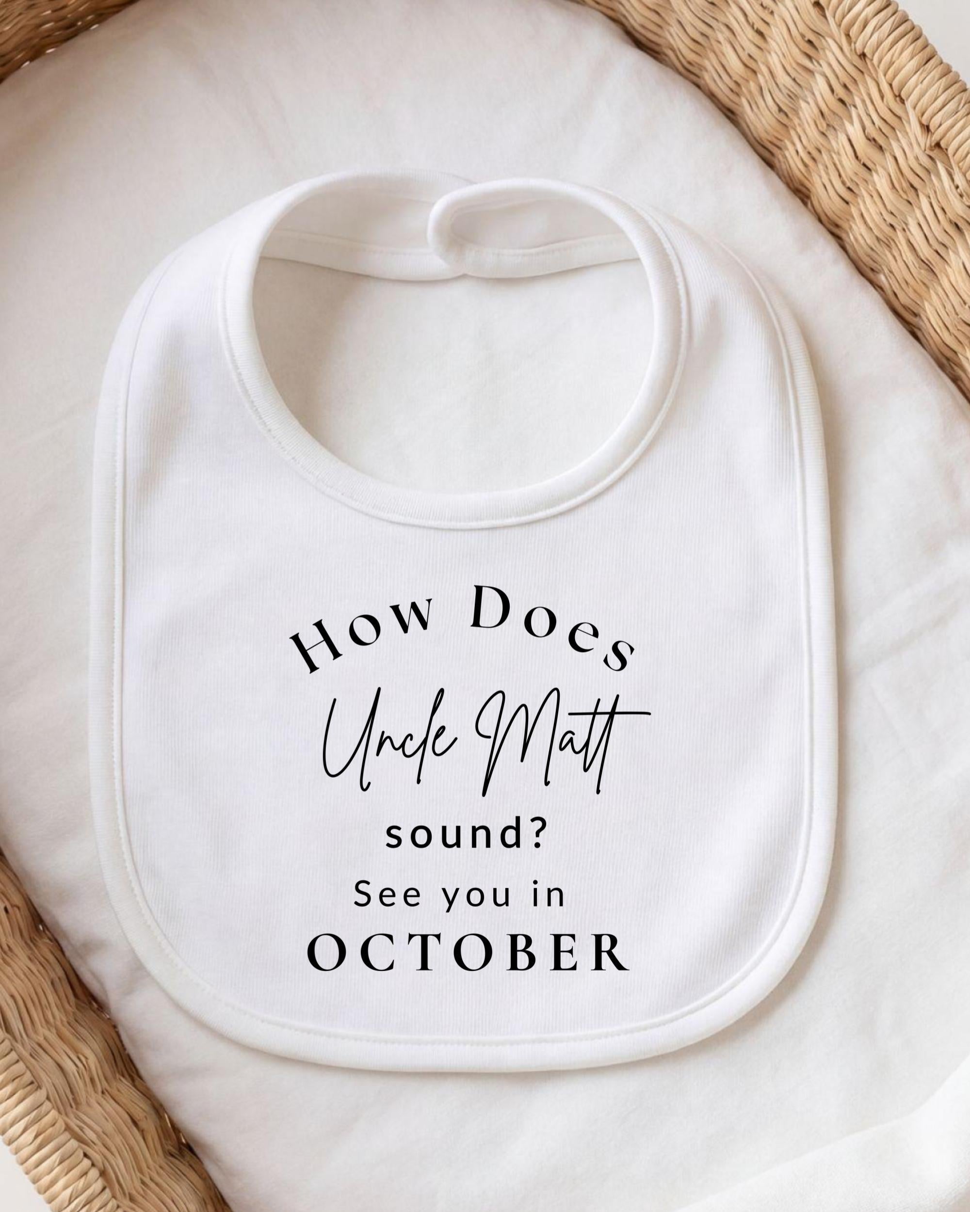 A white bib with text printed on it, placed on a white cloth or blanket.