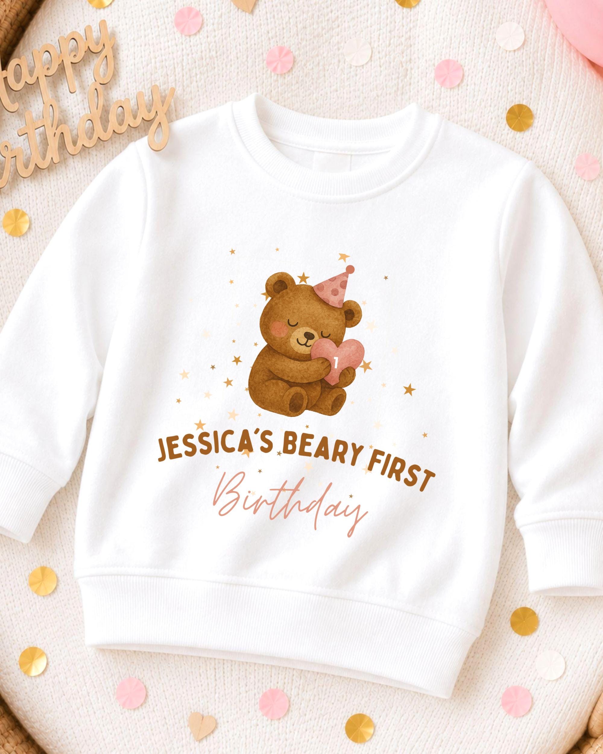 A white sweatshirt with a teddy bear and a birthday hat printed on it, along with the text " Jessica's Beary First Birthday".