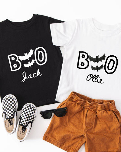 A black t-shirt with the text "BOO Jack" and a white t-shirt with the text "BOOollie" printed on them, along with a pair of brown shorts and a pair of black and white checkered shoes.