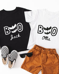 A black t-shirt with the text "BOO Jack" and a white t-shirt with the text "BOOollie" printed on them, along with a pair of brown shorts and a pair of black and white checkered shoes.