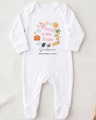 A white onesie with a graphic design on it, featuring various travel-related icons such as a suitcase, a plane, and a palm tree.