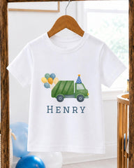 A white t-shirt with a green truck and balloons printed on it, hanging on a wooden hanger.