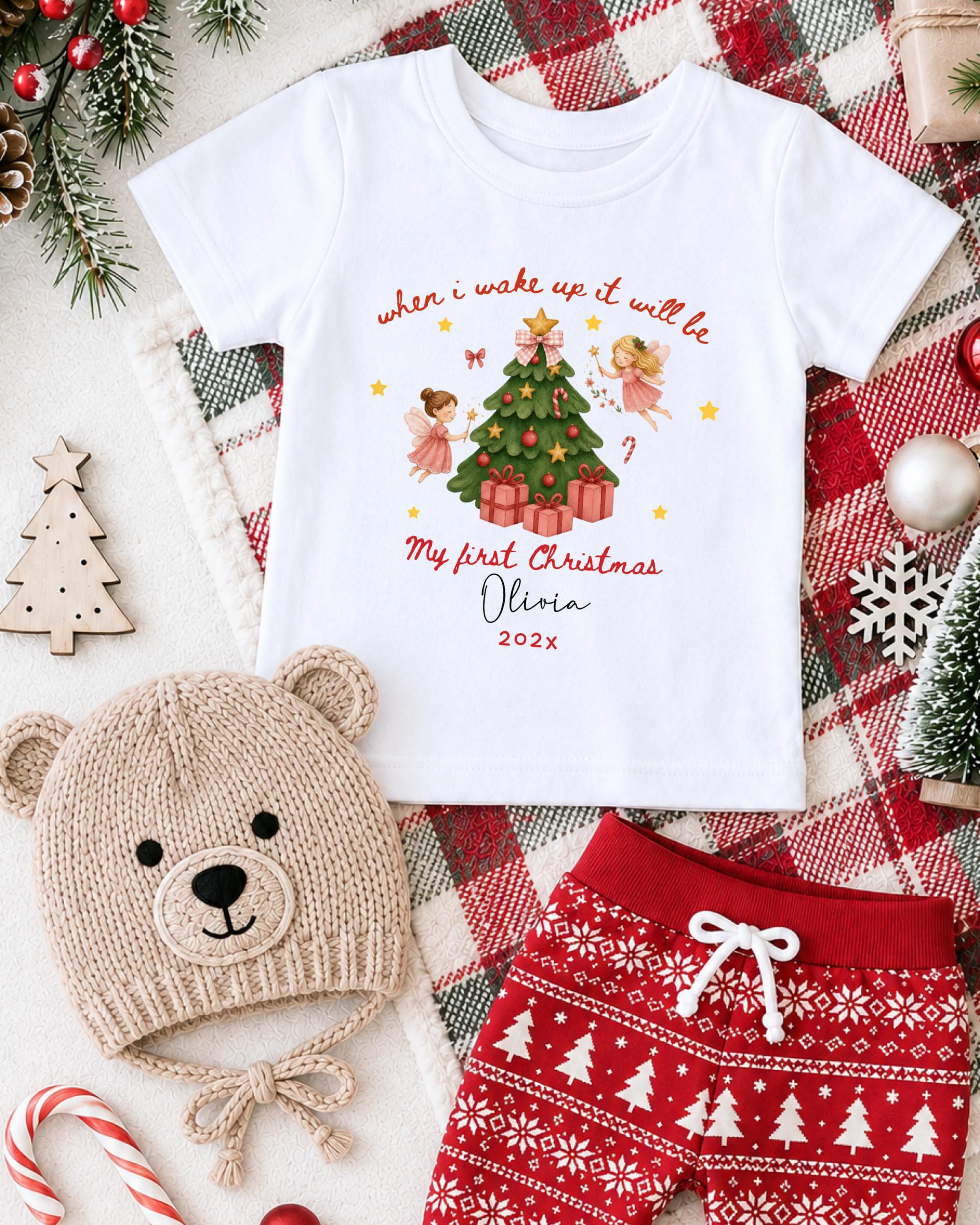 A white t-shirt with a Christmas-themed design, a beige knit hat, red and white patterned shorts, and other Christmas-themed items are arranged on a plaid blanket.